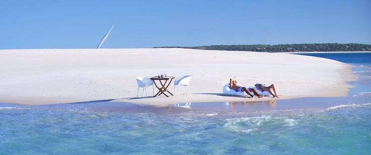 Private sandbar picnic for two on a Zanzibar sandbank, turquoise water and a distant sailboat